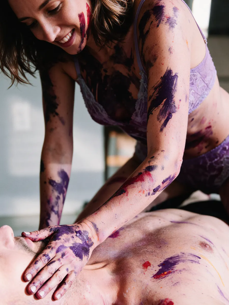 A woman covered in purple paint painting her partner's body — an evening with the NakedArt kit